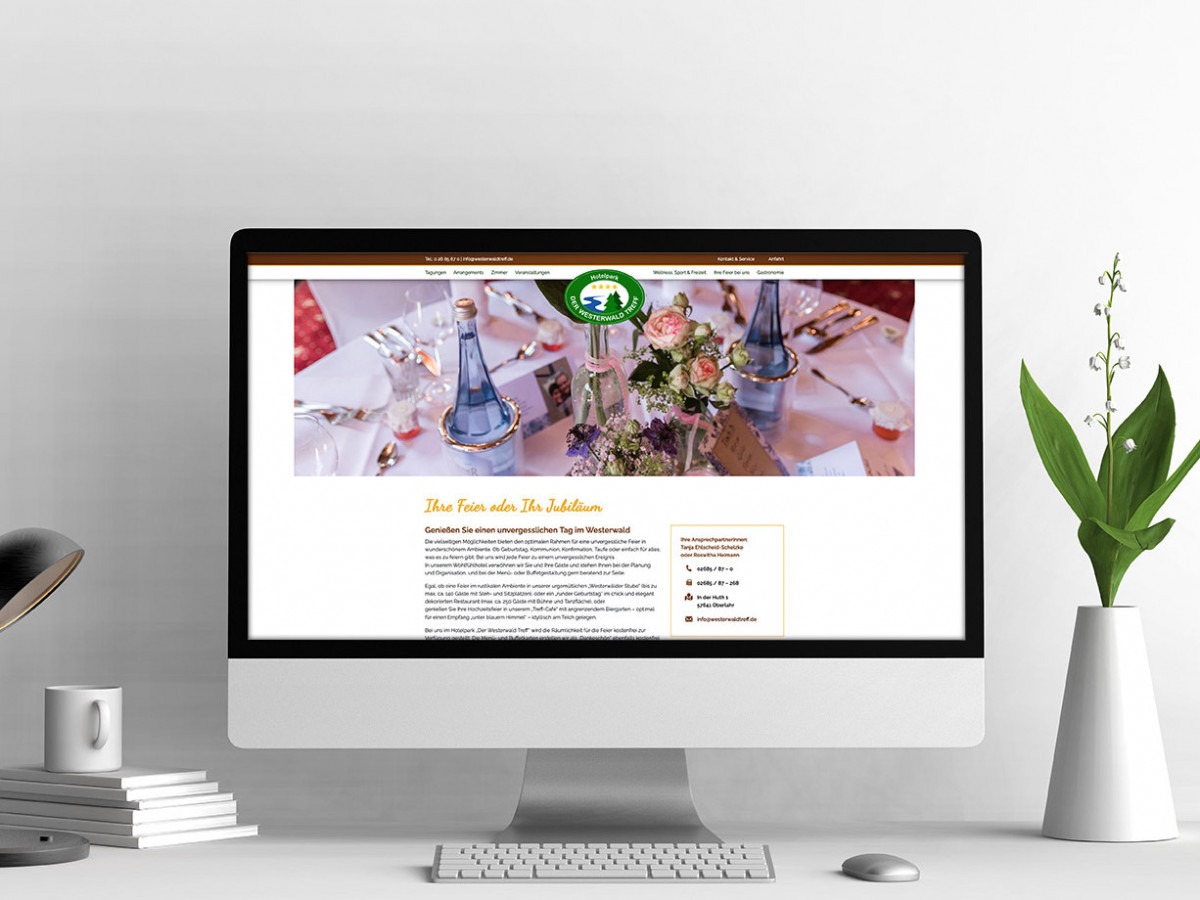 Computerbildschirm zeigt eine Webseite mit einem gedeckten Tisch, Blumenarrangement und zwei blauen Flaschen in der Mitte.